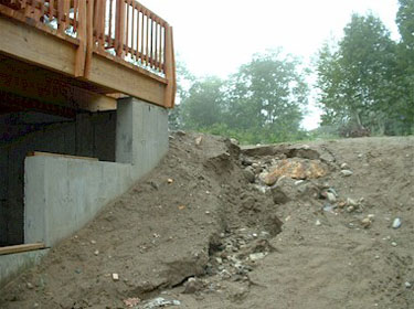 Dirt slope eroding downhill past a deck of a house.